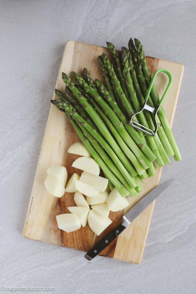 peeled asparagus and potatoes on cutting board with peeler and knife