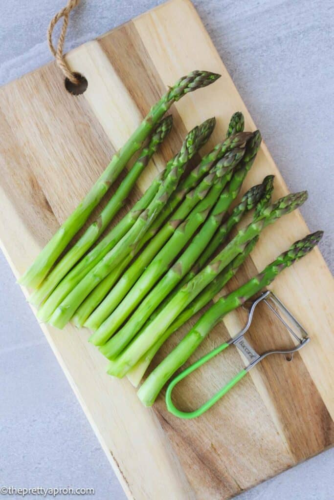 peeled asparagus on cutting board with peeler