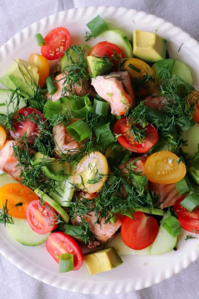 salmon, cucumber, baby tomatoes, dill, spring onion layerd on cooked quinoa on white plate