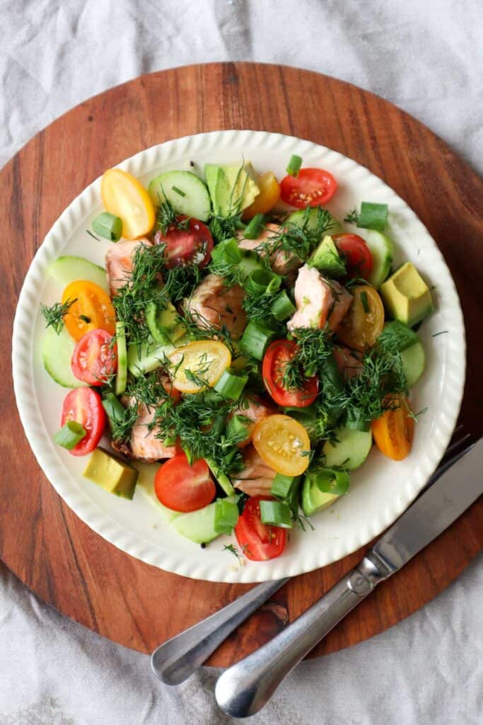 quinoa layered with salmon, spinach, tomatoes, cucumbers, spring onions and dill and parsley and salad dressing