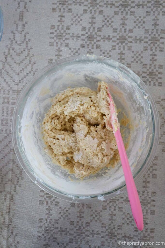 Adding dry ingredients to wet muffin ingredients in a glass bowl with a pink spatula.