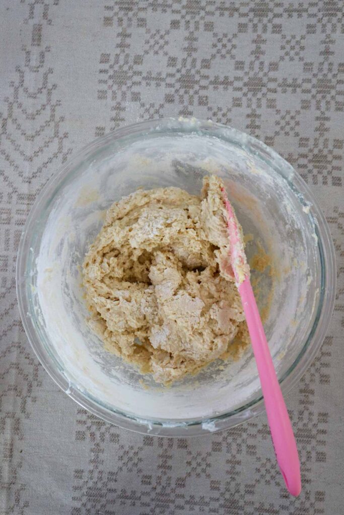 Adding dry ingredients to wet muffin ingredients in a glass bowl with a pink spatula.