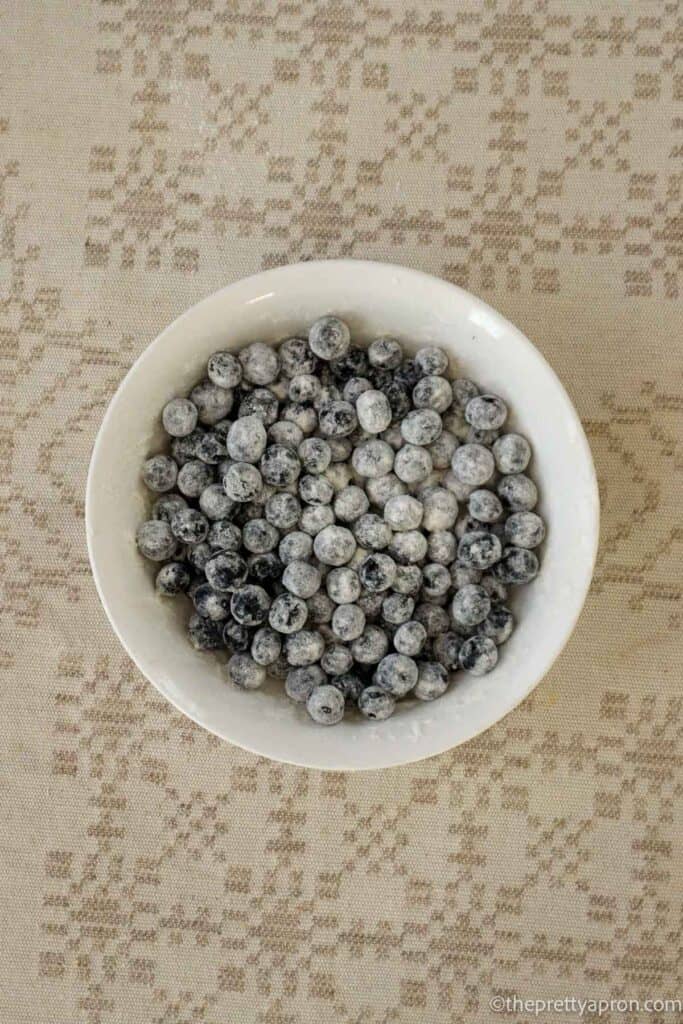 Blueberries in a white bowl that are lightly covered with flour.