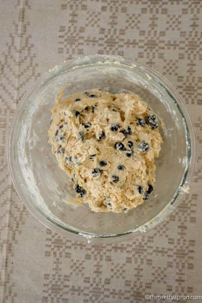 Blueberry cottage cheese muffin batter in glass bowl which is set on a linen tablecloth.