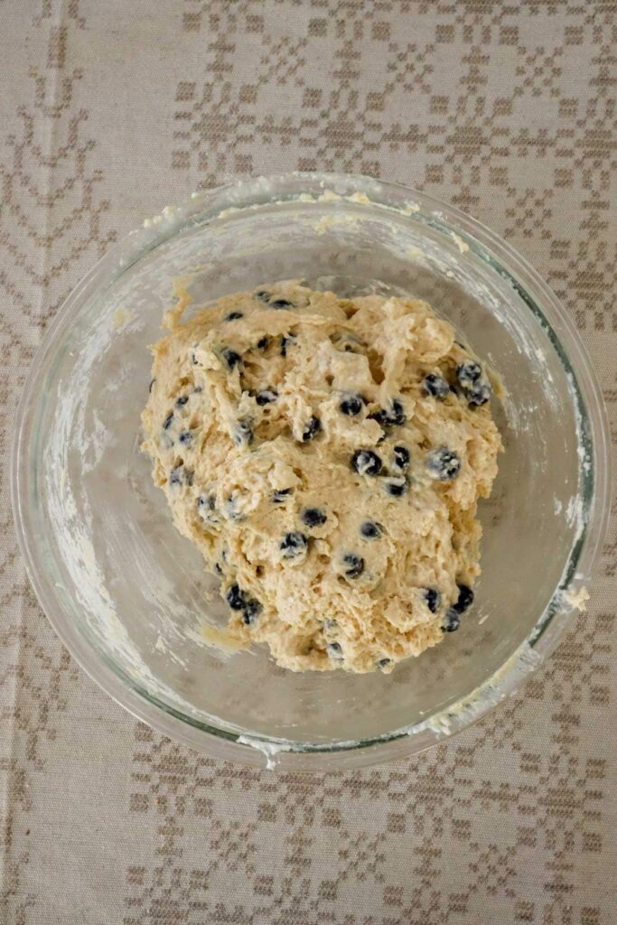 Blueberry cottage cheese muffin batter in glass bowl which is set on a linen tablecloth.