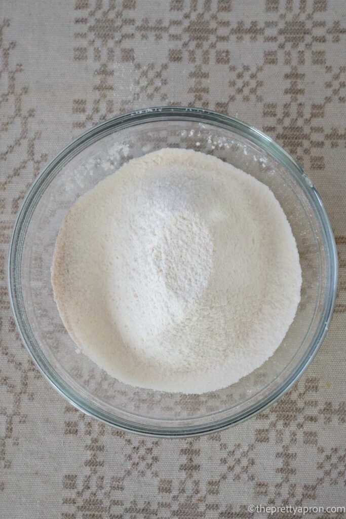Flour, baking soda, baking powder, salt and cinnamon sifted into a glass bowl.
