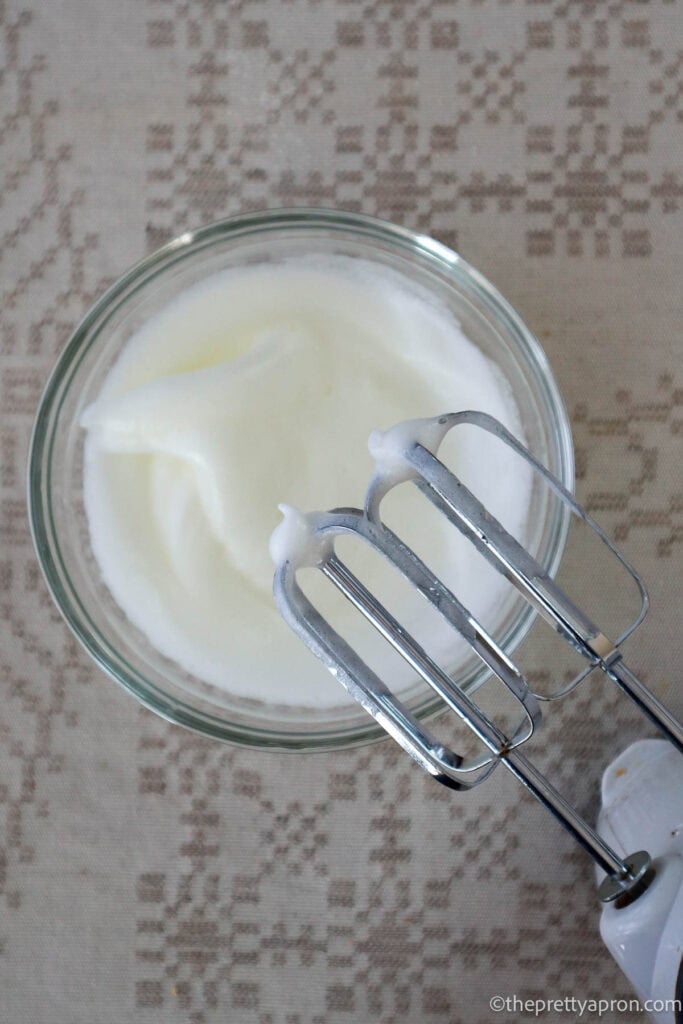 Egg whites beaten in glass bowl on linen tablecloth. You can see the hand held mixer.