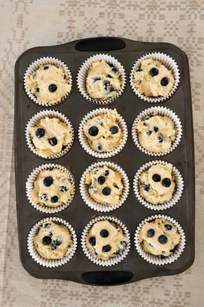 12 blueberry cottage cheese muffins in a muffin tray which is sitting on a linen tablecloth