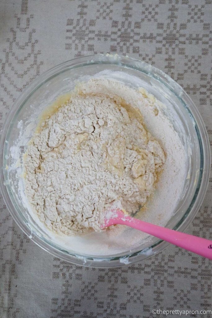 Adding dry ingredients to wet muffin ingredients in a glass bowl with a pink spatula.