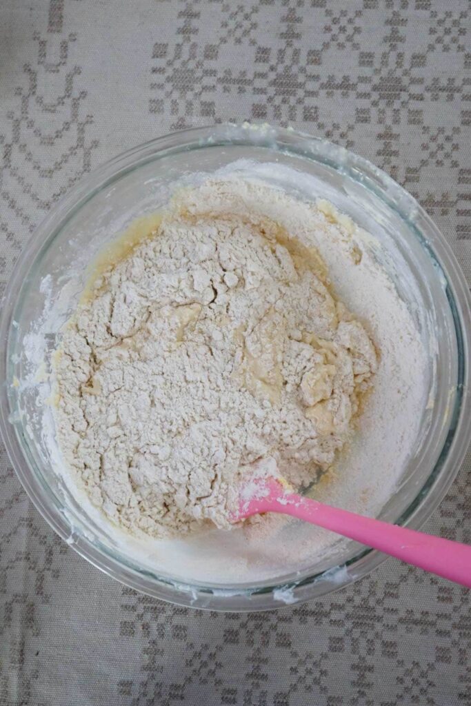 Adding dry ingredients to wet muffin ingredients in a glass bowl with a pink spatula.