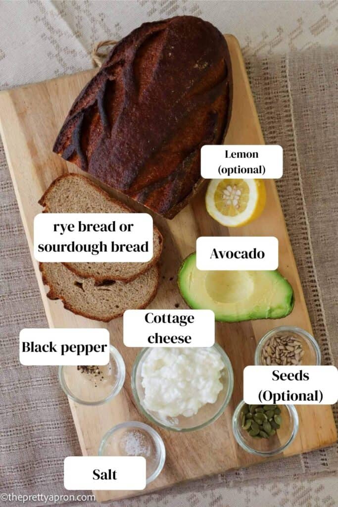 ingredients with rye bread, avocado, lemon, pepper, cottage cheese, avocado, salt and seeds on wooden board
