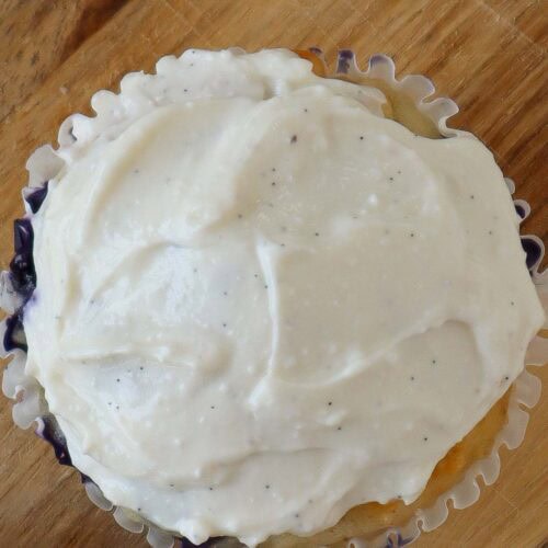 Close up of a muffin with white cottage cheese frosting on top. It is sitting on a wooden cutting board.