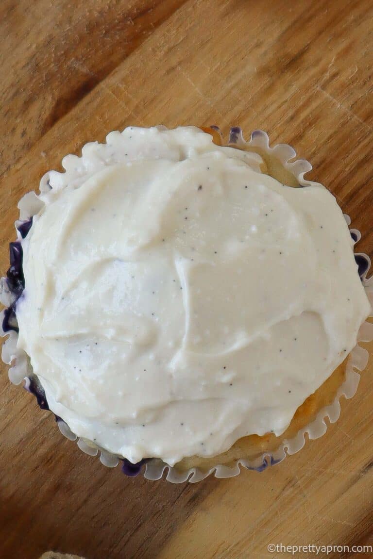 Close up of a muffin with white cottage cheese frosting on top. It is sitting on a wooden cutting board.