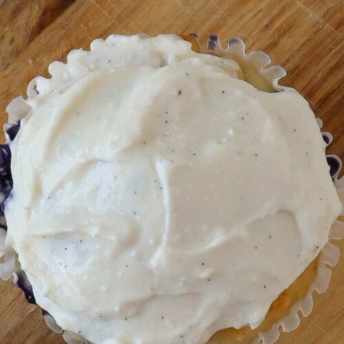 Close up of a muffin with white cottage cheese frosting on top. It is sitting on a wooden cutting board.