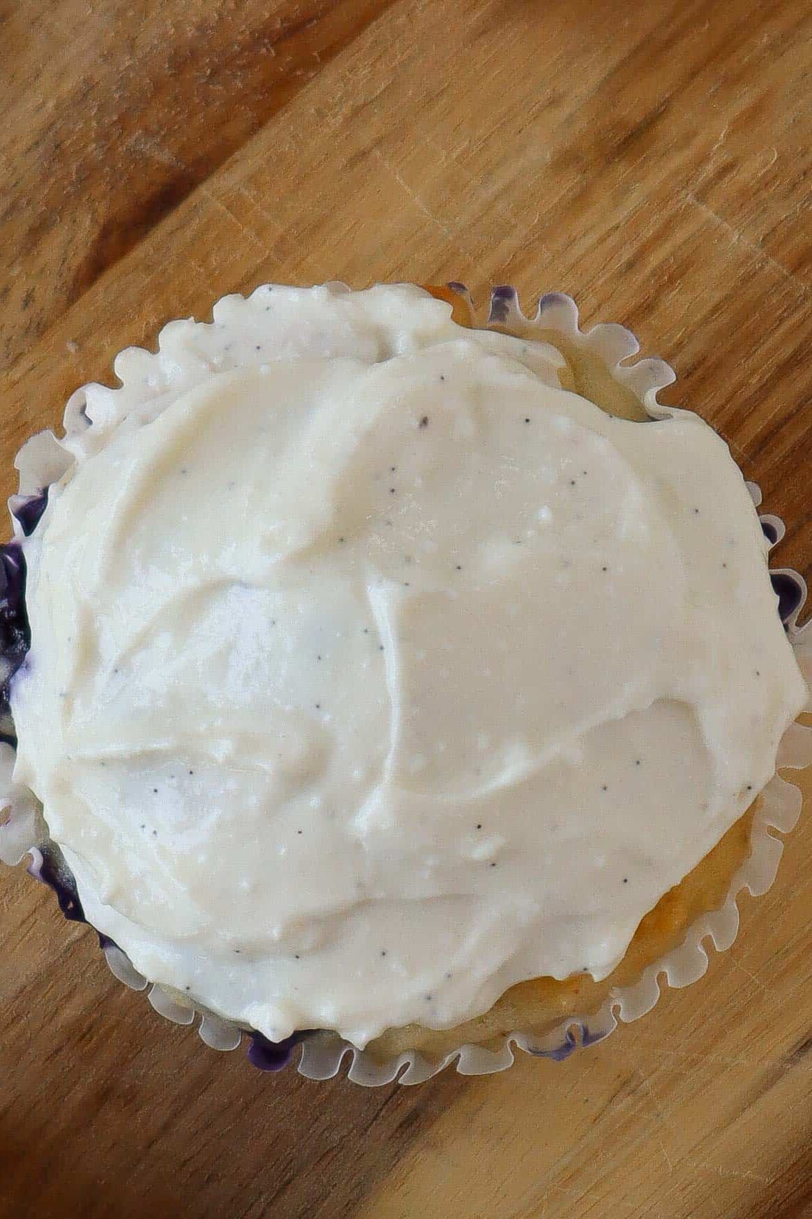 Close up of a muffin with white cottage cheese frosting on top. It is sitting on a wooden cutting board.
