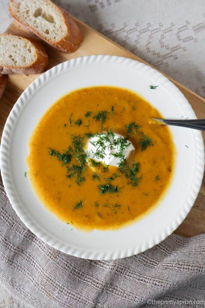 Pumpkin Cauliflower soup in white bowl. The soup is sprinkled with chopped dill and has a scoop of cream cheese in the middle.