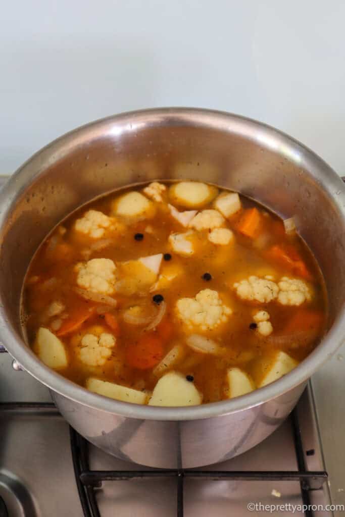 Pumpkin, cauliflower, potatoes, apple, onion, carrot, garlic and spices boiling in a medium pot.