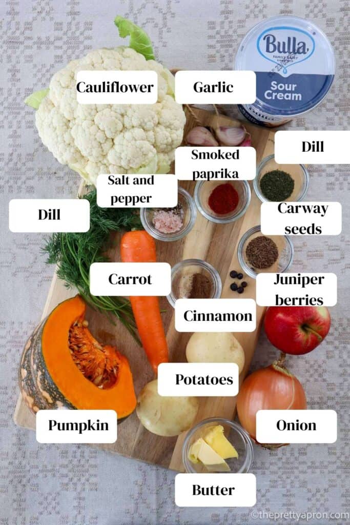 Cauliflower, pumpkin, carrot, onion, potatoes, apple, juniper berries, salt and pepper, cinnamon, smoked paprika, garlic, caraway seeds, sour cream place on cutting board. these are the ingredients for pumpkin and cauliflower soup.