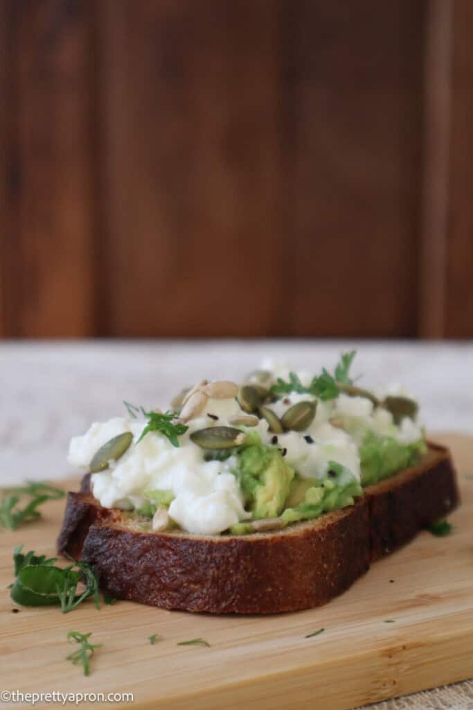cottage cheese avocado toast with toasted seeds on wooden board