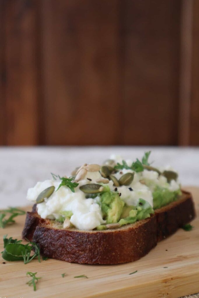 cottage cheese avocado toast with toasted seeds on wooden board