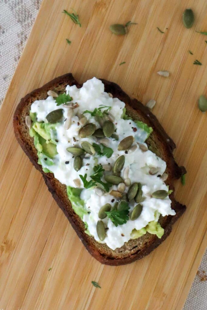cottage cheese avocado toast with toasted pumpkin and sunflower seeds on wooden board