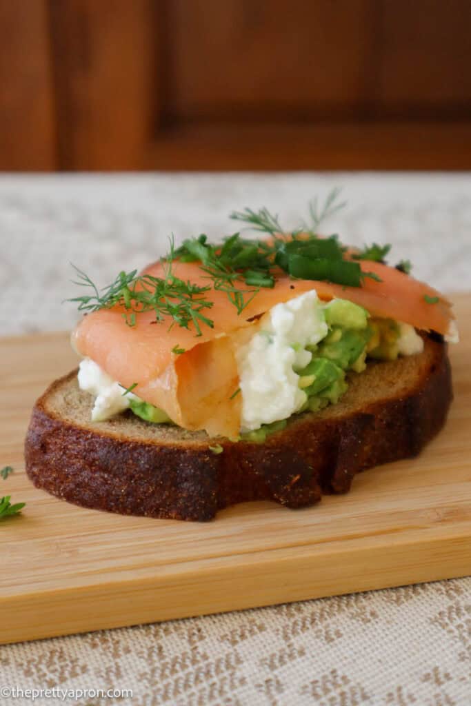 cottage cheese avocado toast with smoked salmon and dill, chives and spring onion on wooden board