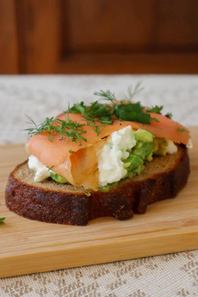 cottage cheese avocado toast with smoked salmon and dill, chives and spring onion on wooden board