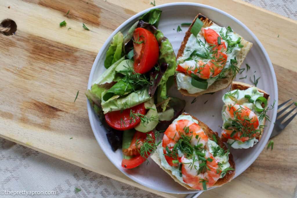 shrimp avocado toast on plate with garden salad and plate on wooden board