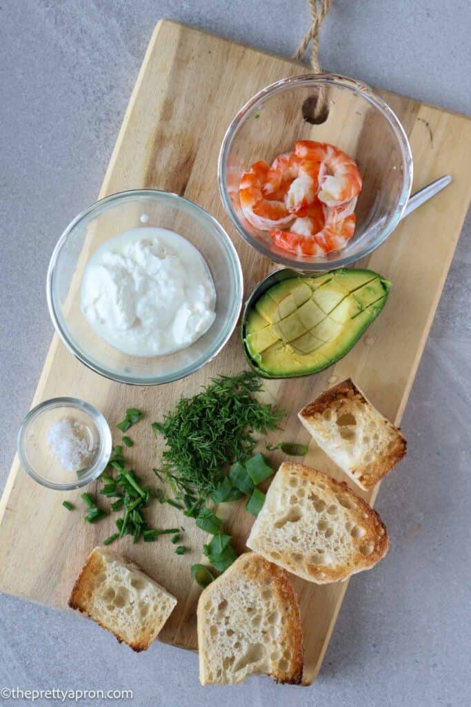 cleaned shrimnp, greek yogurt, half avocado, chopped herbs and toast on wooden board