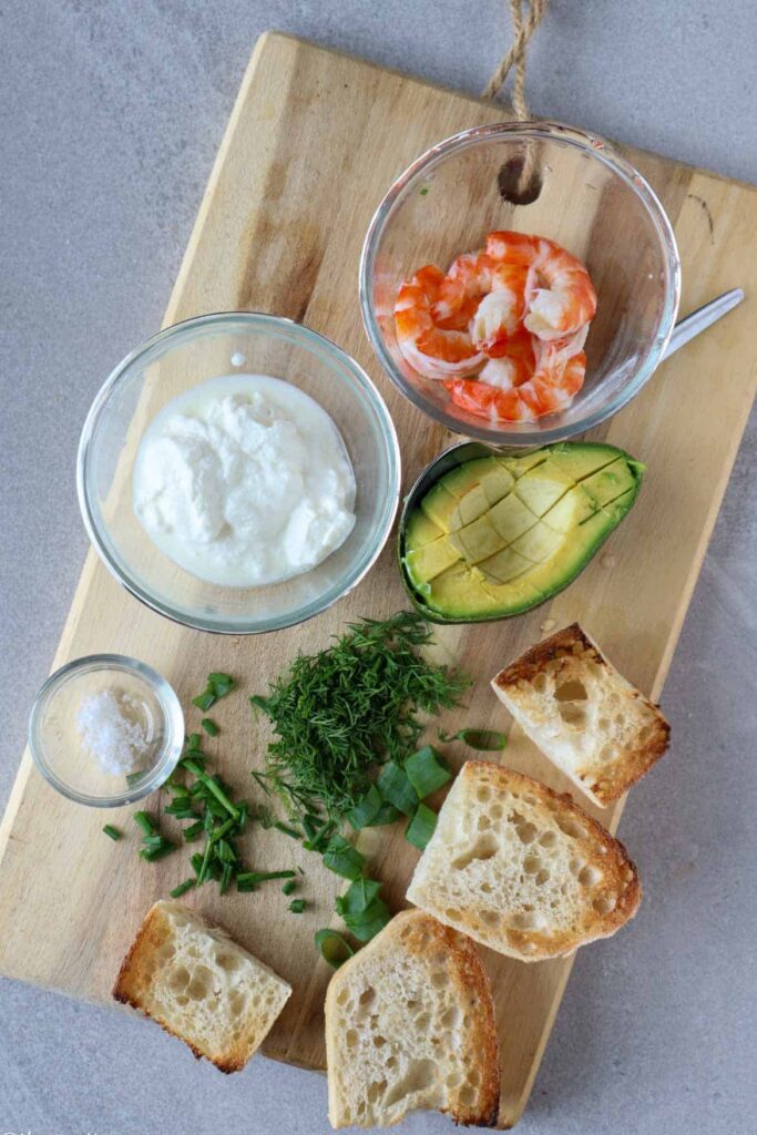 cleaned shrimnp, greek yogurt, half avocado, chopped herbs and toast on wooden board