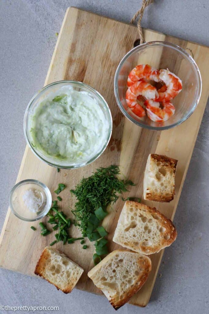 avocado mixed with yogurt, shrimp, herbs and toast on wooden board