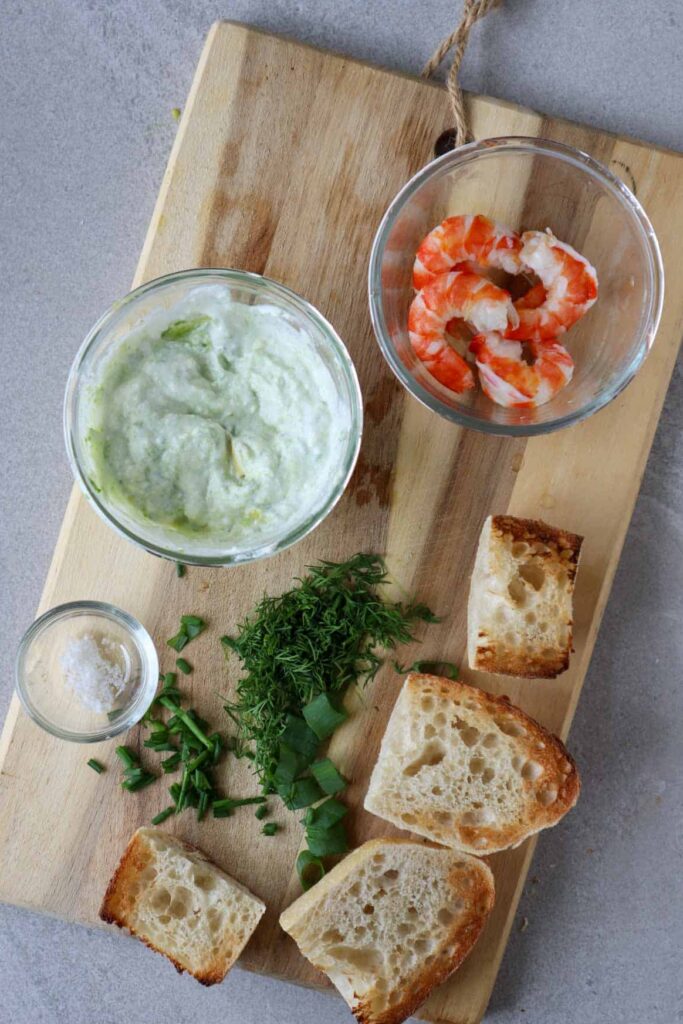 avocado mixed with yogurt, shrimp, herbs and toast on wooden board