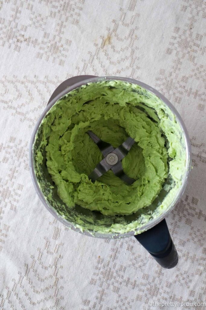 Green creamy dip mixture in a thermomix blender, which is placed on a linen tablecloth