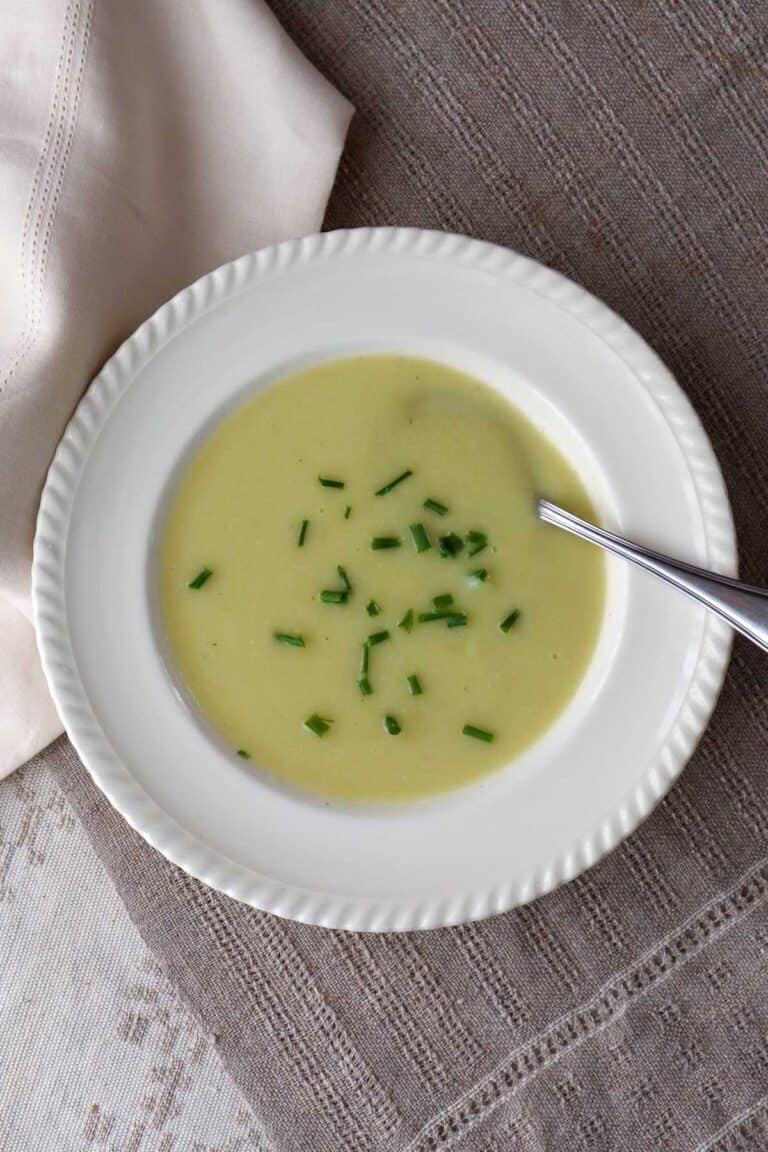 Cauliflower, leek and potato soup with sprinkles of green chives in beige sop bowl. The bowl is on a linen tablecloth.