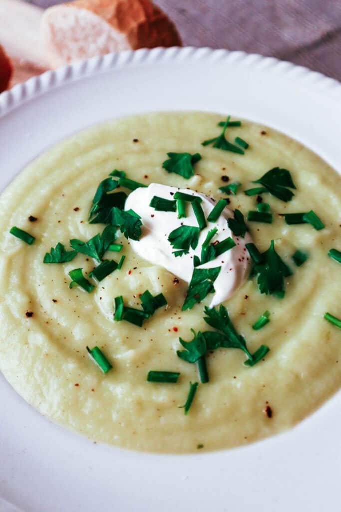 cauliflower, potato and leek soup in white bowl with parsley garnish and dollop of creme fraiche.