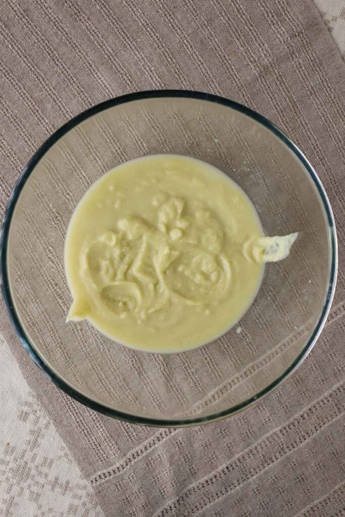 Smooth cauliflower, leek and potato soup in a glass bowl, which is placed on a linen tablecloth.