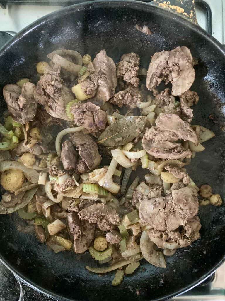 chicken livers, onion, celery, parsnip, bay leaf simmering in a skillet.