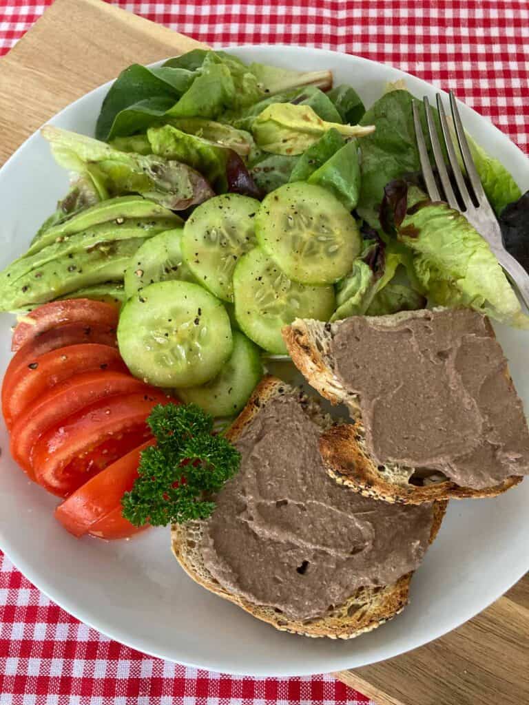 Chicken liver pate on bread on a pate with lettuce, cucumbers, tomatoes and avocado.