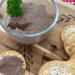 Chicken liver pâté in glass bowl on a wooden cutting board with water crackers.