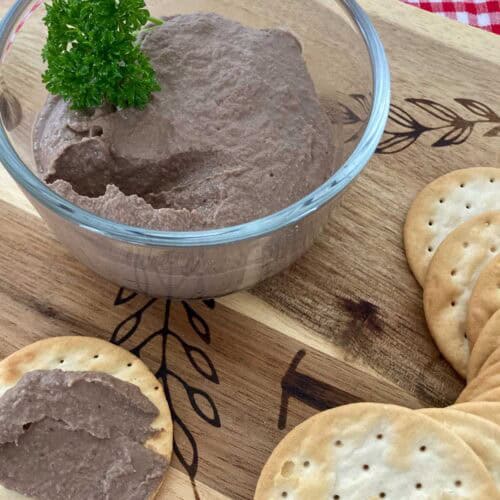 Chicken liver pâté in glass bowl on a wooden cutting board with water crackers.