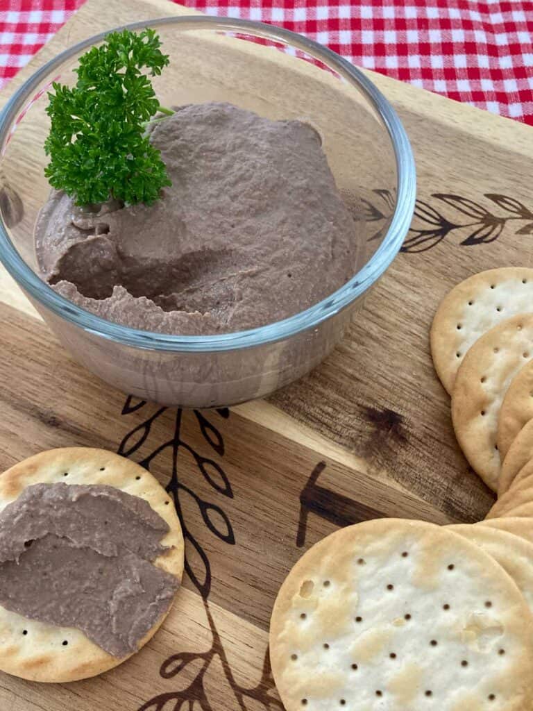 Chicken liver pâté in glass bowl on a wooden cutting board with water crackers.