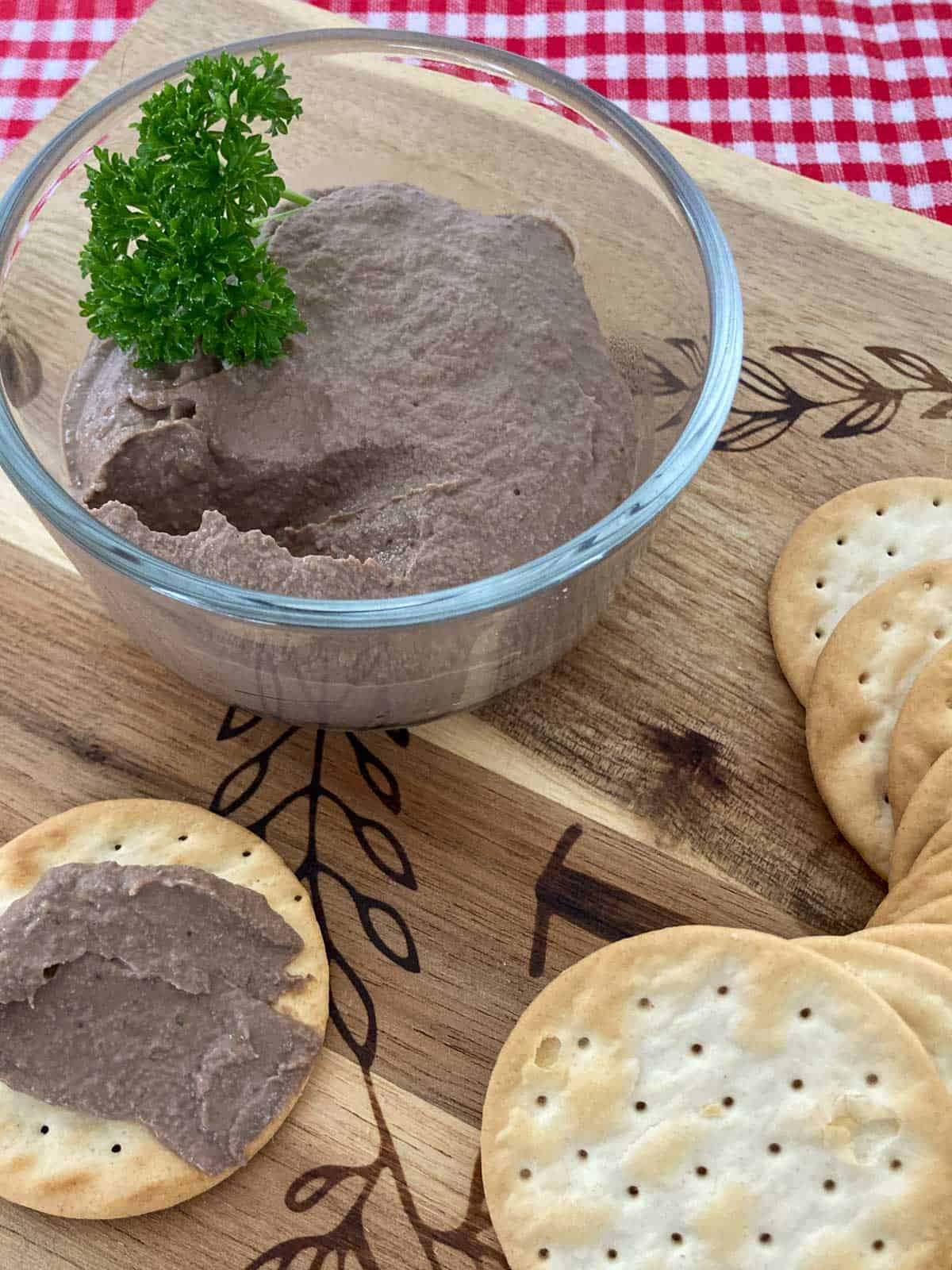 Chicken liver pâté in glass bowl on a wooden cutting board with water crackers.