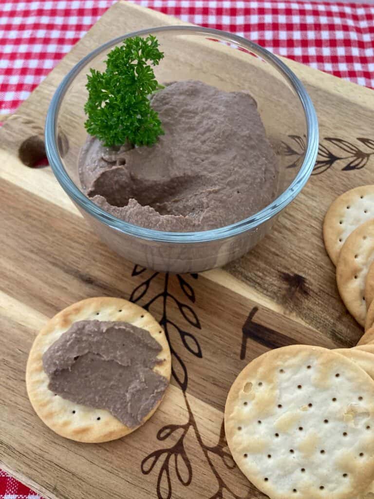 Chicken liver pâté in glass bowl on a wooden cutting board with water crackers.