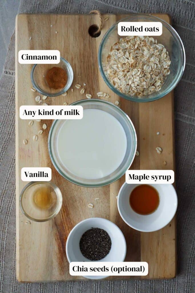 Oats, milk, cinnamon, vanilla, chia seeds and maple syrup in small glass bowls on a wooden board.
