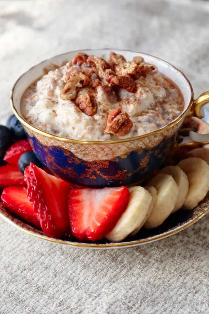 Cinnamon roll overnight oats in blue teacup with strawberries, bananas, blueberries and nuts in the saucer.