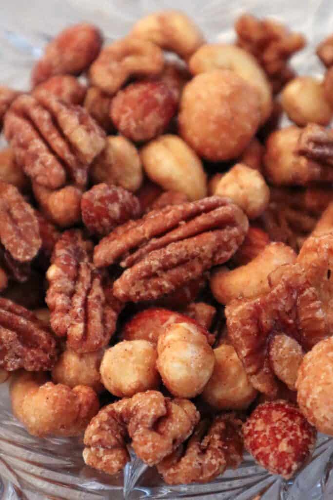 Maple syrup roasted nut mix including pecans, walnuts, hazelnuts, cashews, macadamia nuts and almonds served in a glass bowl.
