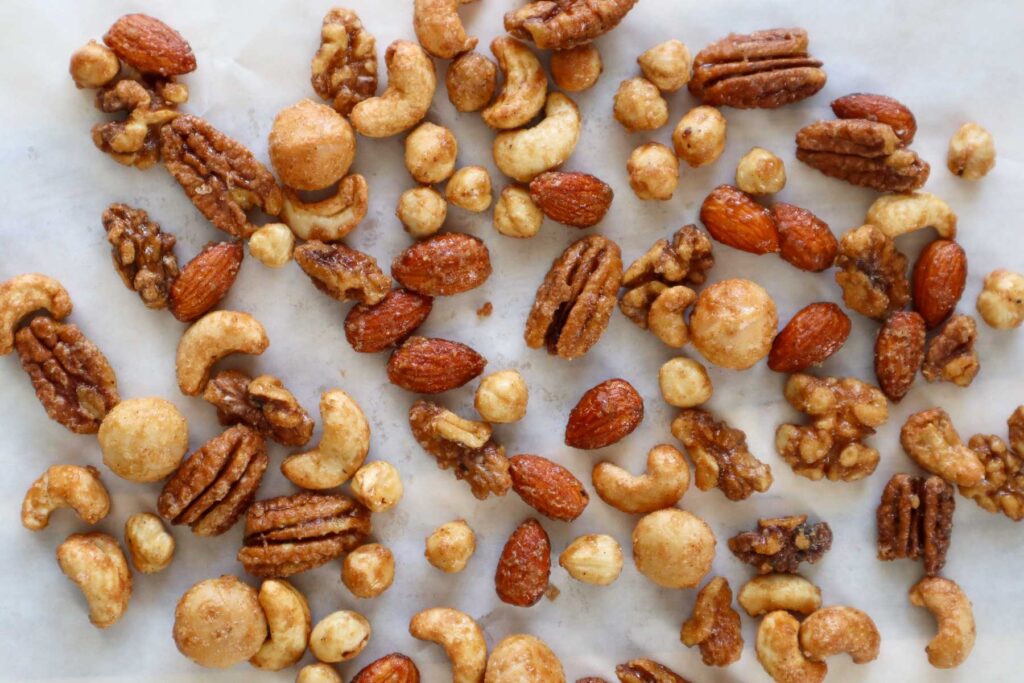 Mixed roasted nuts on parchment paper, including maple pecans, maple walnuts, maple macadamia nuts, maple hazelnuts and maple cashews.
