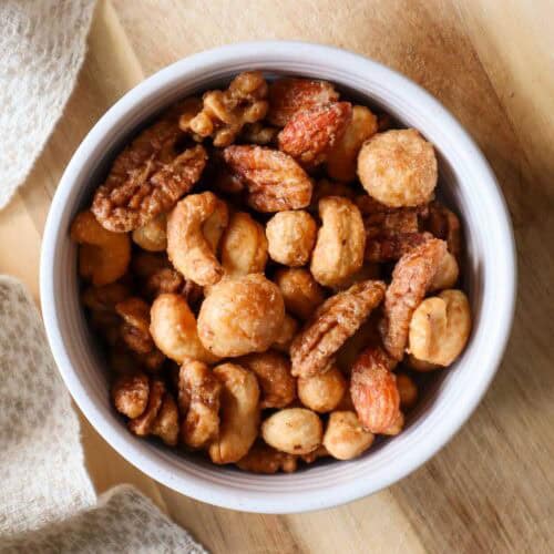 Golden roasted mixed nut bowl with walnuts, cashews, almonds, and pecans on wooden surface, perfect for snacks.