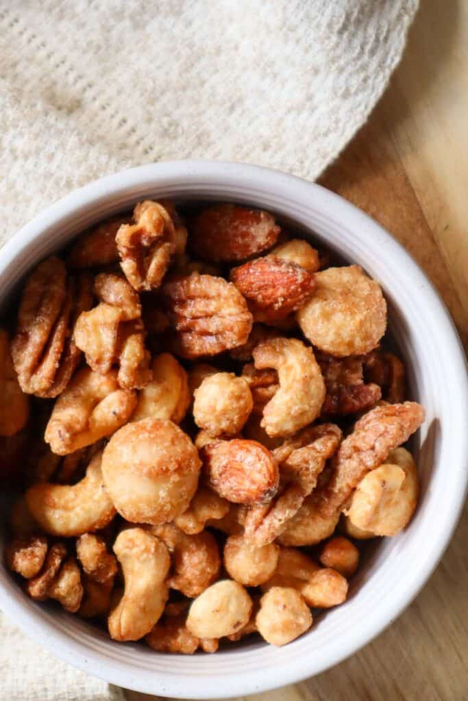 Maple mixed nuts in a white bowl on wooden surface, gourmet snack.
