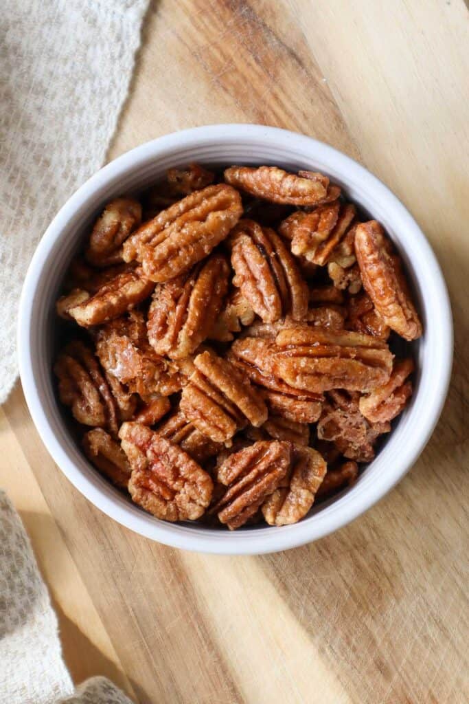 Maple roasted pecans in a beige bowl on a wooden board.